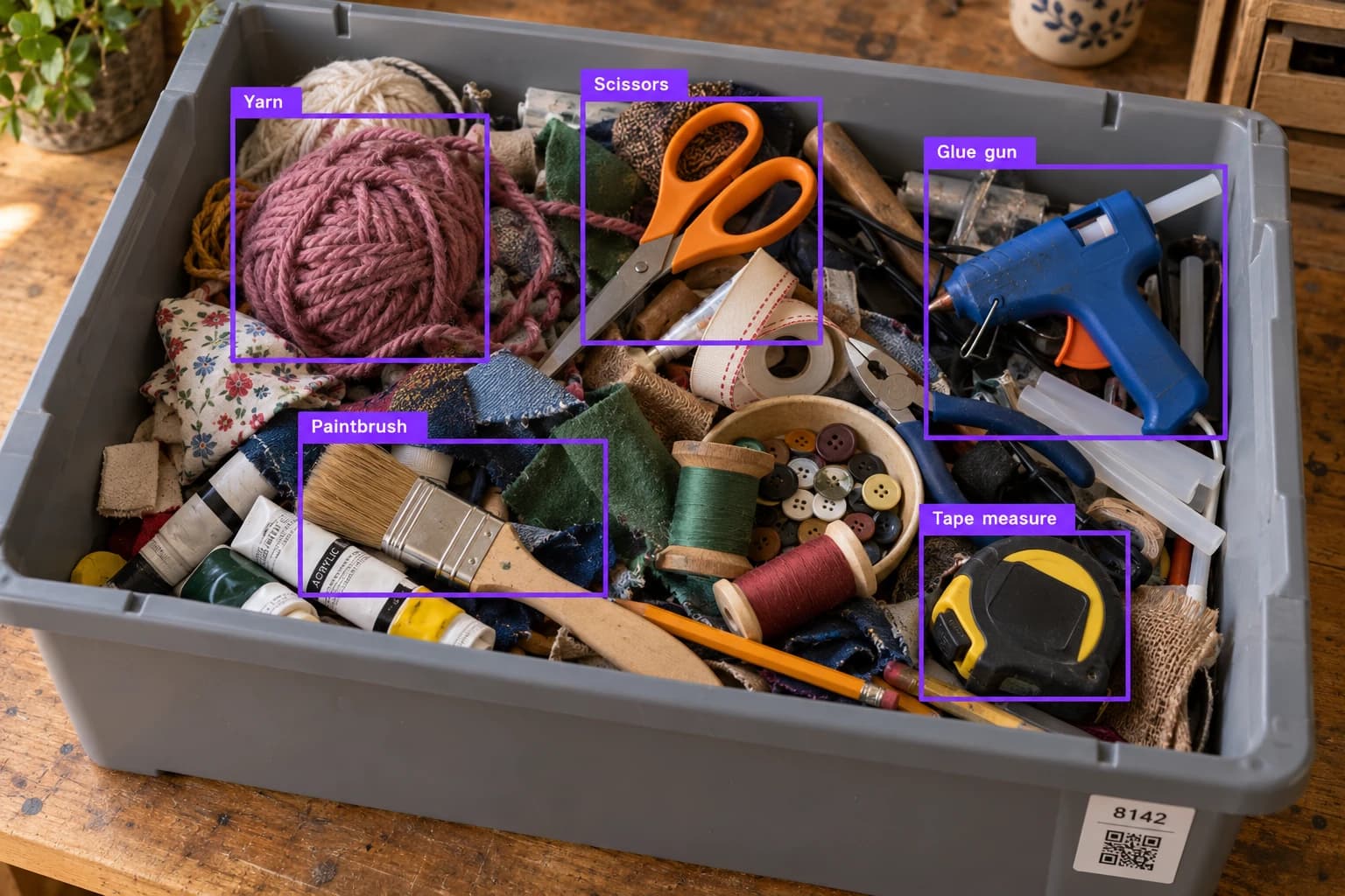 A messy bin of craft supplies and tools with image-recognition boxes identifying yarn, scissors, a glue gun, a paintbrush, and a tape measure